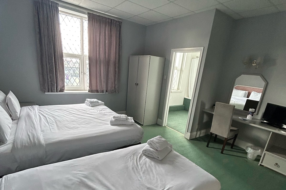 A hotel room with two beds, a desk, a chair, a wardrobe, and a window with curtains.