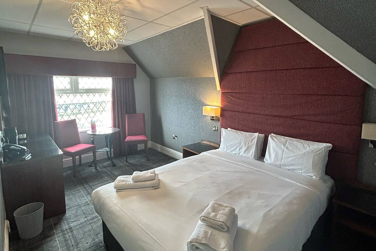 A hotel room with a large bed, a desk with a chair, a small table, and a chandelier.