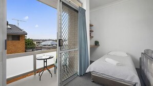 A bedroom with a bed, a small table, and a chair. There is a balcony with a view of the outside.