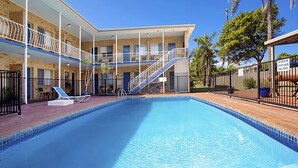 A swimming pool with a covered area, a staircase, and a fenced balcony.