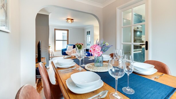 A dining area with a long wooden table set for six, a blue chair, and a vase with flowers. - 2 Bed in Braunton (oc-stepco) (Braunton)