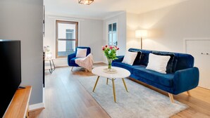 A modern living room with a blue sofa, a white coffee table, and a TV. - 2 Bed in Braunton (oc-stepco) (Braunton)