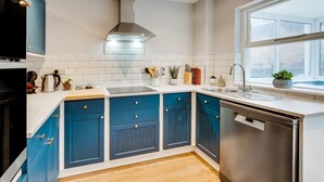 A modern kitchen with blue cabinets, a stainless steel range hood, and a dishwasher. - 2 Bed in Braunton (oc-stepco) (Braunton)