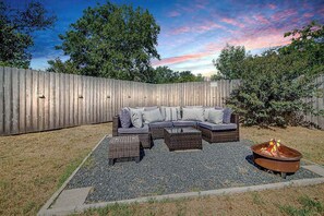 An outdoor seating area with a sofa and ottomans, a fire pit, and a wooden fence. - Charming Getaway 4 Min to Downtown-Hot Tub, Firepit Grill (Fredericksburg)