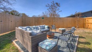 Ein Garten mit einer Korbsitzgruppe, einem runden Tisch und Metallstühlen.