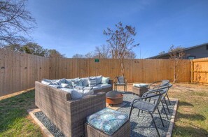 A backyard with a wicker sofa set, a round table, and metal chairs.