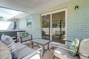 Eine Terrasse mit einem Glastisch, gepolsterten Stühlen und einer Glasschiebetür zu einem Außenbereich.