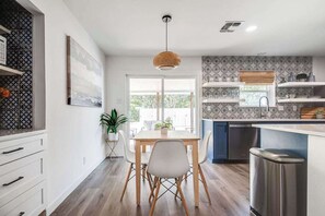 A modern kitchen with a dining table, chairs, and a hanging light fixture.