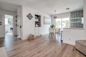 Una cocina moderna con armarios blancos, un comedor con mesa y sillas, y un amplio ventanal que proporciona luz natural.