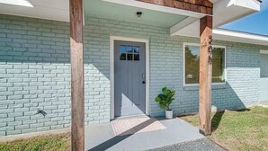 Ein Haus mit hellblauer Ziegelöberzug, einer weißen Tür und einem kleinen Blumentopf auf der Veranda.