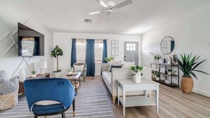 Ein modernes Wohnzimmer mit einer Couch, einem blauen Sessel, einem Couchtisch und einem an der Wand befestigten Fernseher.