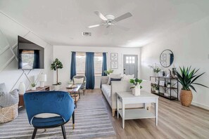 A modern living room with a sofa, a blue chair, a coffee table, and a TV mounted on the wall.