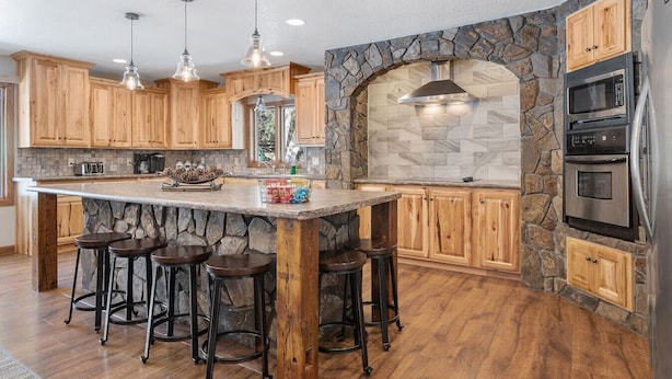 A kitchen with wooden cabinets, a stone arch, and a central island with stools.