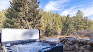 A hot tub with a stone wall backdrop, surrounded by trees.