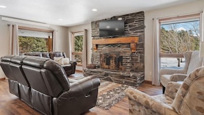 A living room with a stone fireplace, leather recliner, and patterned armchair.