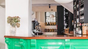 A bar area with a green bar counter, three stools, a hanging light fixture, and a view into the kitchen area. - The Bull Inn (Totnes)