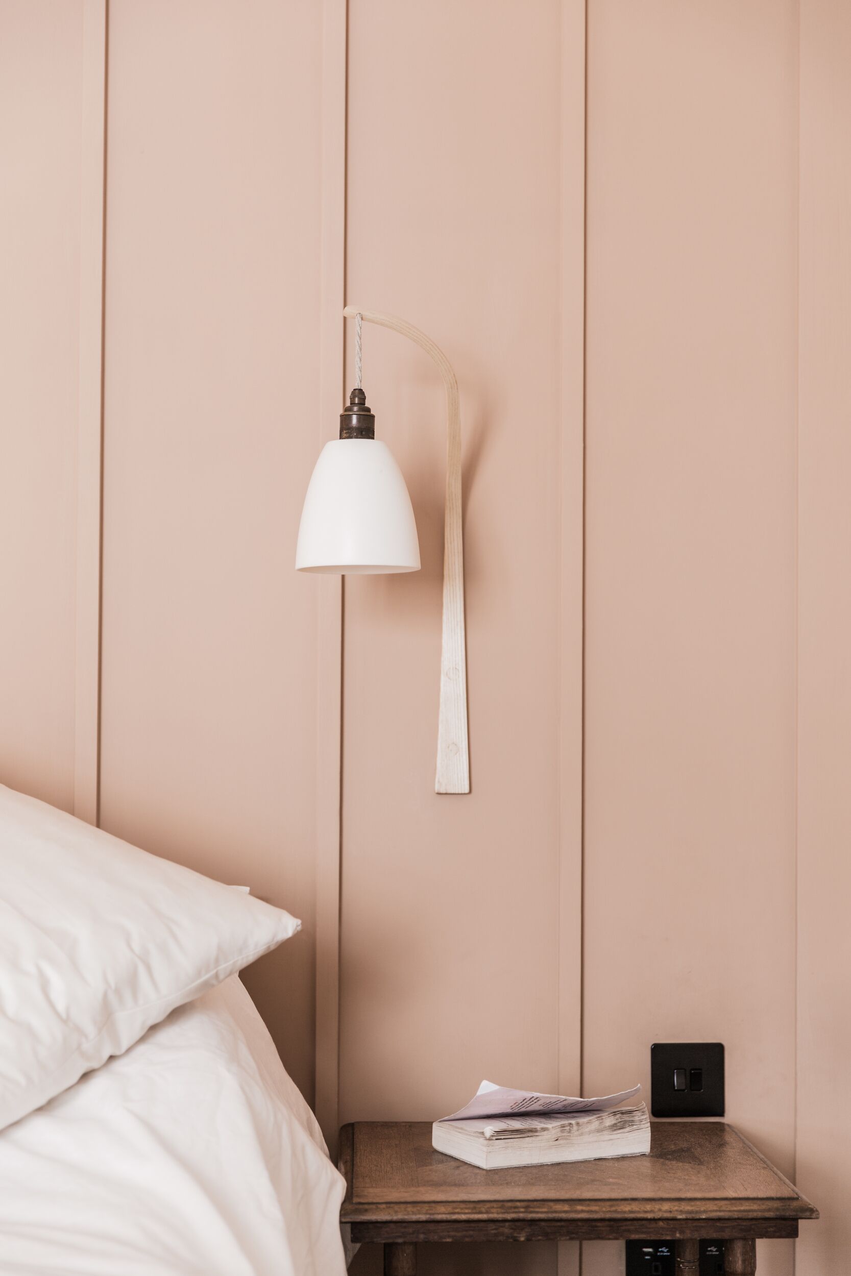 A bedroom with a bed, a bedside table with a lamp, and a wall socket.