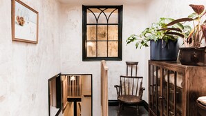 A narrow hallway with a wooden chair, a cabinet with glass doors, and a window with a decorative frame. - The Bull Inn (Totnes)