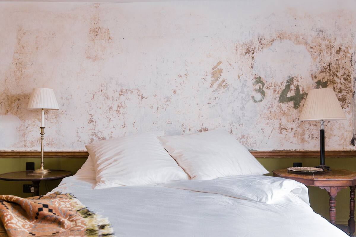 A bed with white linens, two bedside tables with lamps, and a wall with a distressed finish and a number '34' painted on it.