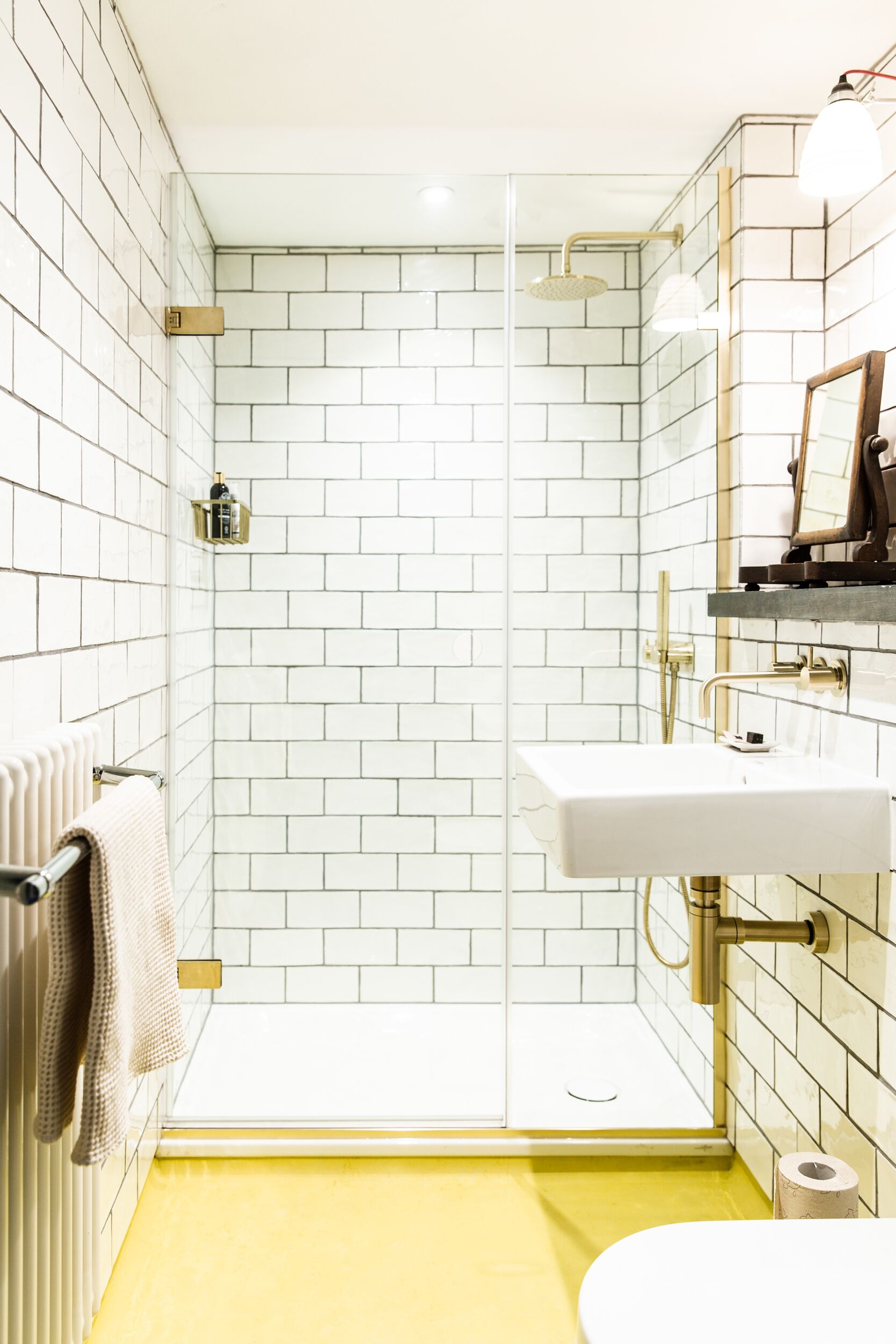 A bathroom with white subway tiles, a yellow floor, a white sink, and a glass-enclosed shower.