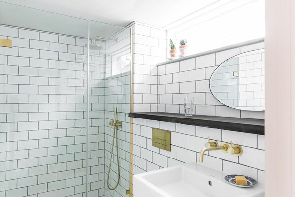 A modern bathroom with white subway tiles, a glass-enclosed shower, a gold faucet, and a small shelf with potted plants. - The Bull Inn (Totnes)