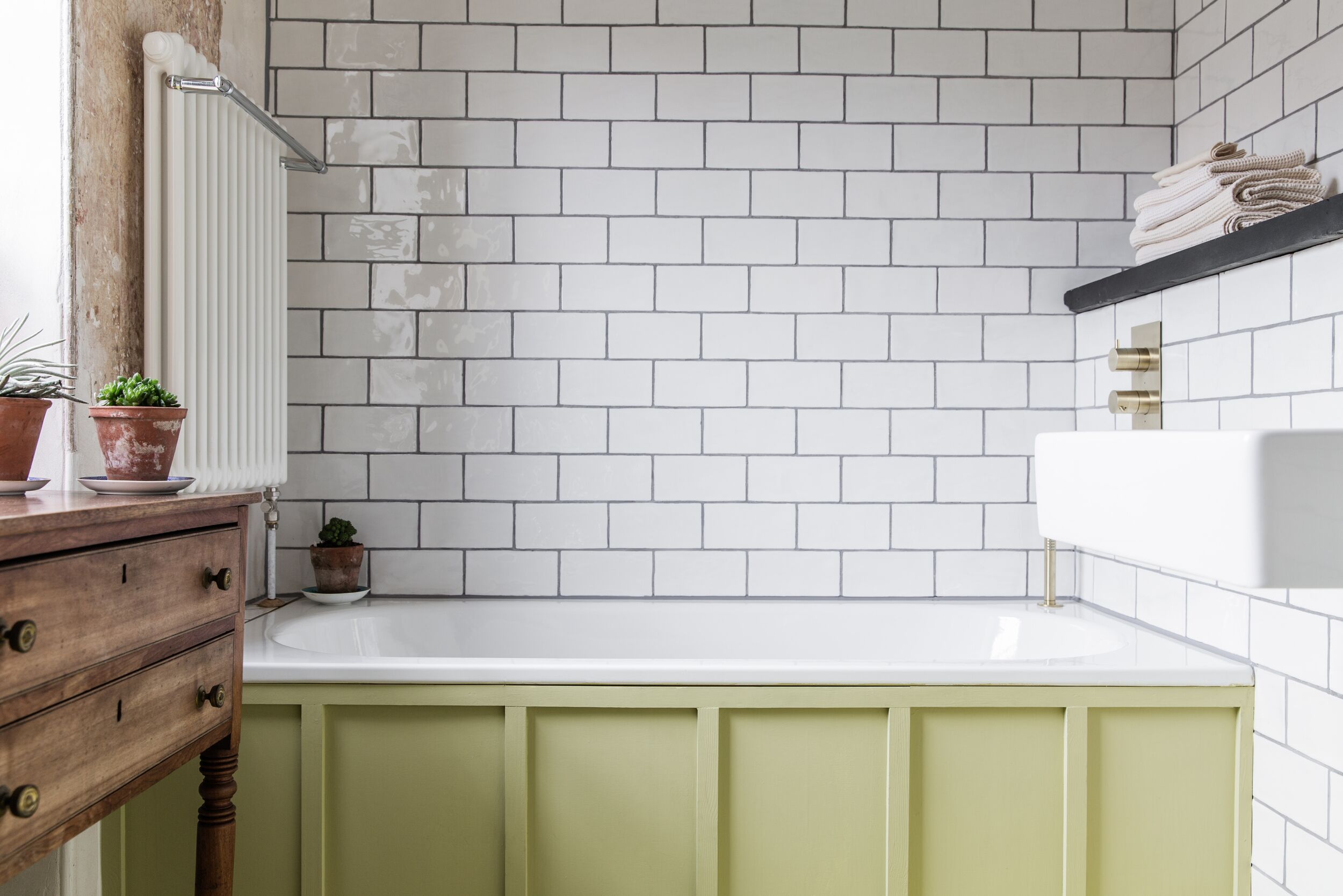 A bathroom with white subway tiles, a white sink, a green vanity, and a radiator.