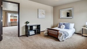 A bedroom with a bed, a bedside table, a mirror, a shelf with folded clothes, and a window with curtains.