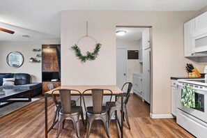 A modern kitchen with white cabinets, a wooden dining table, and a hanging wreath.