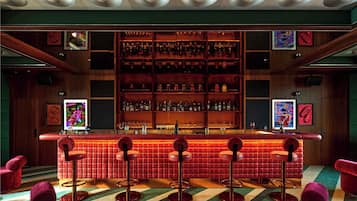 A bar area with a red-tiled counter, multiple stools, and shelves stocked with bottles.