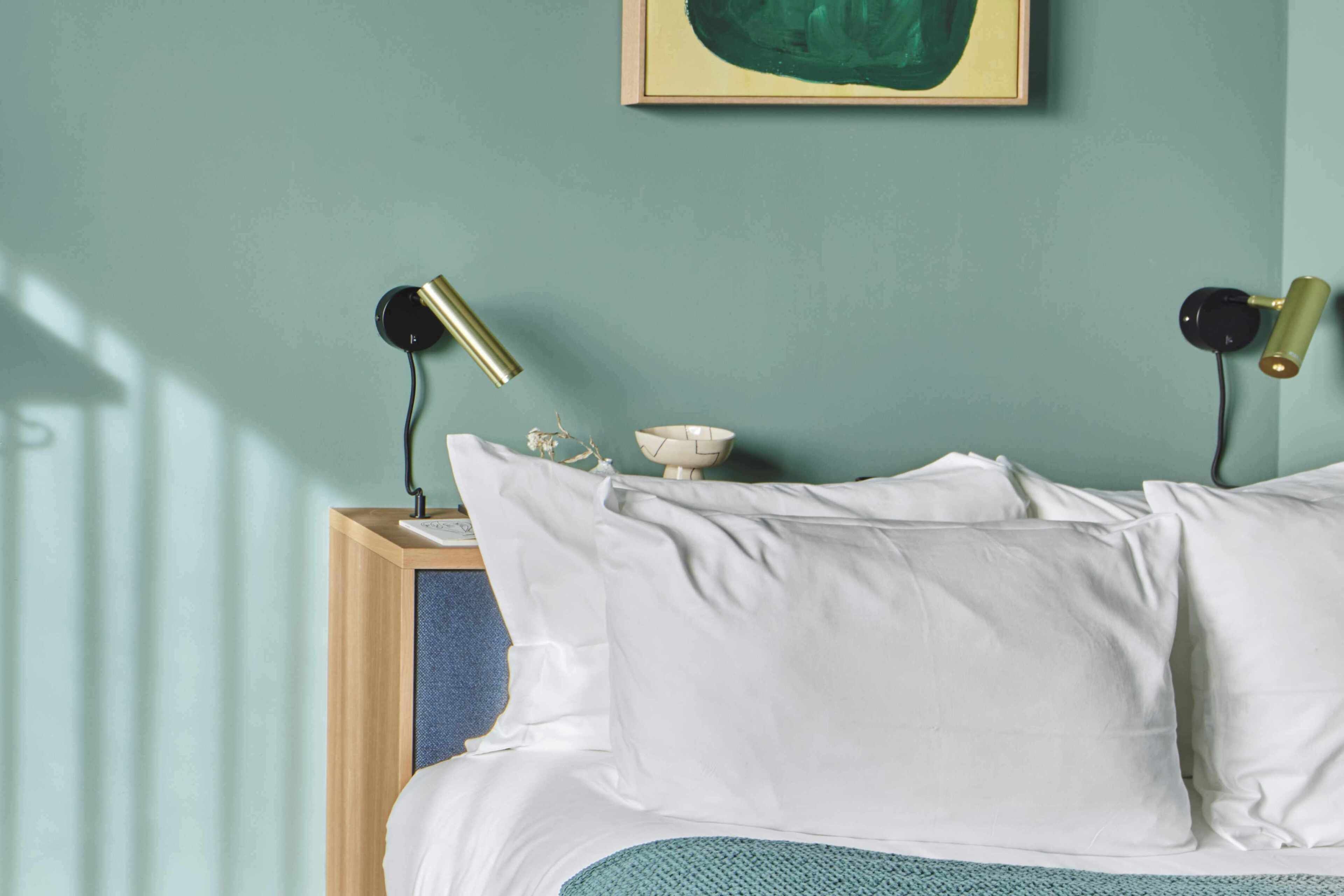 Una cama con ropa blanca, un cuenco blanco pequeño y dos lámparas negras con pantallas doradas.