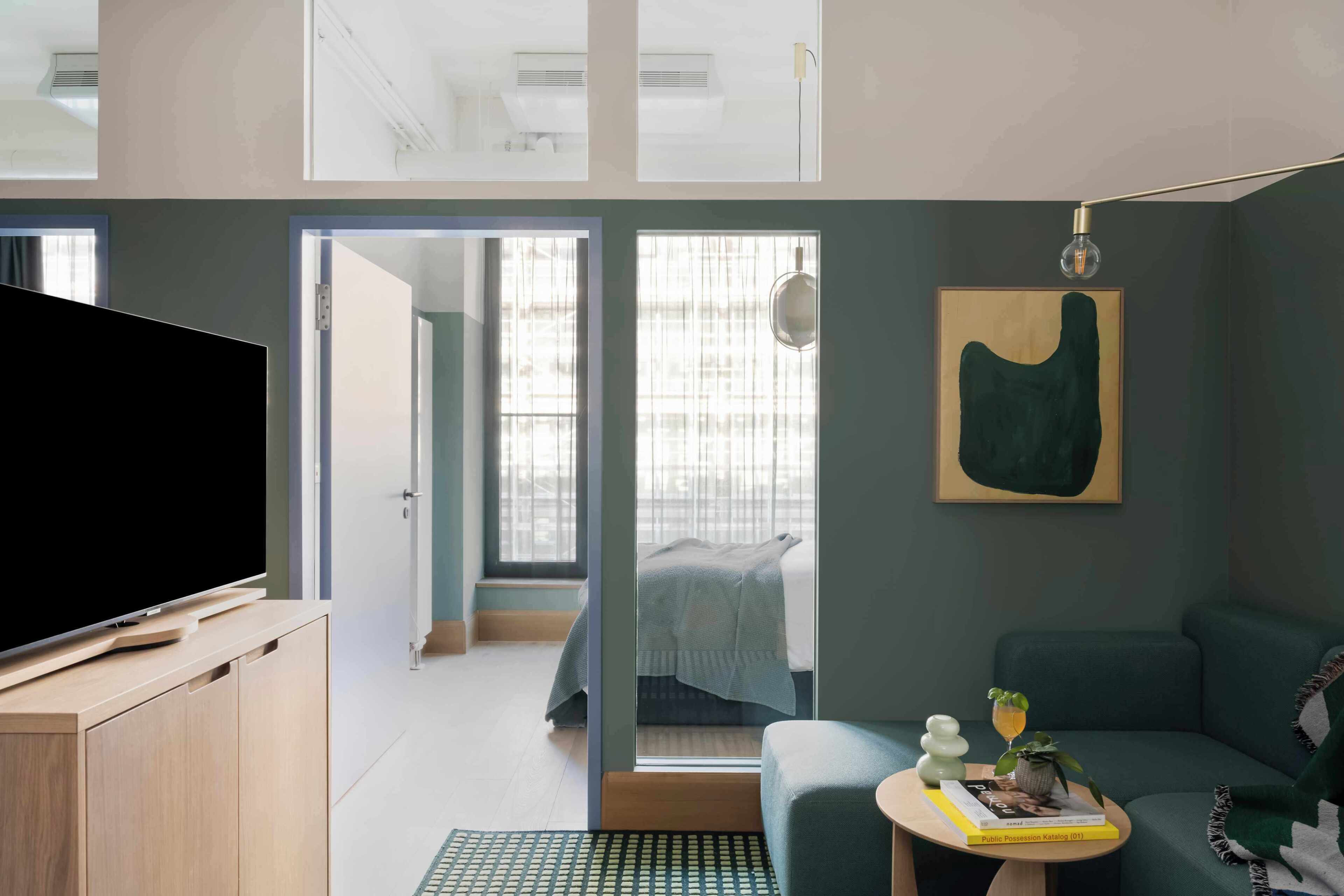 Ein modernes Zimmer mit Flachbildfernseher, einer Couch, einem kleinen Tisch mit Buch und Pflanze sowie einem Bild an der Wand.