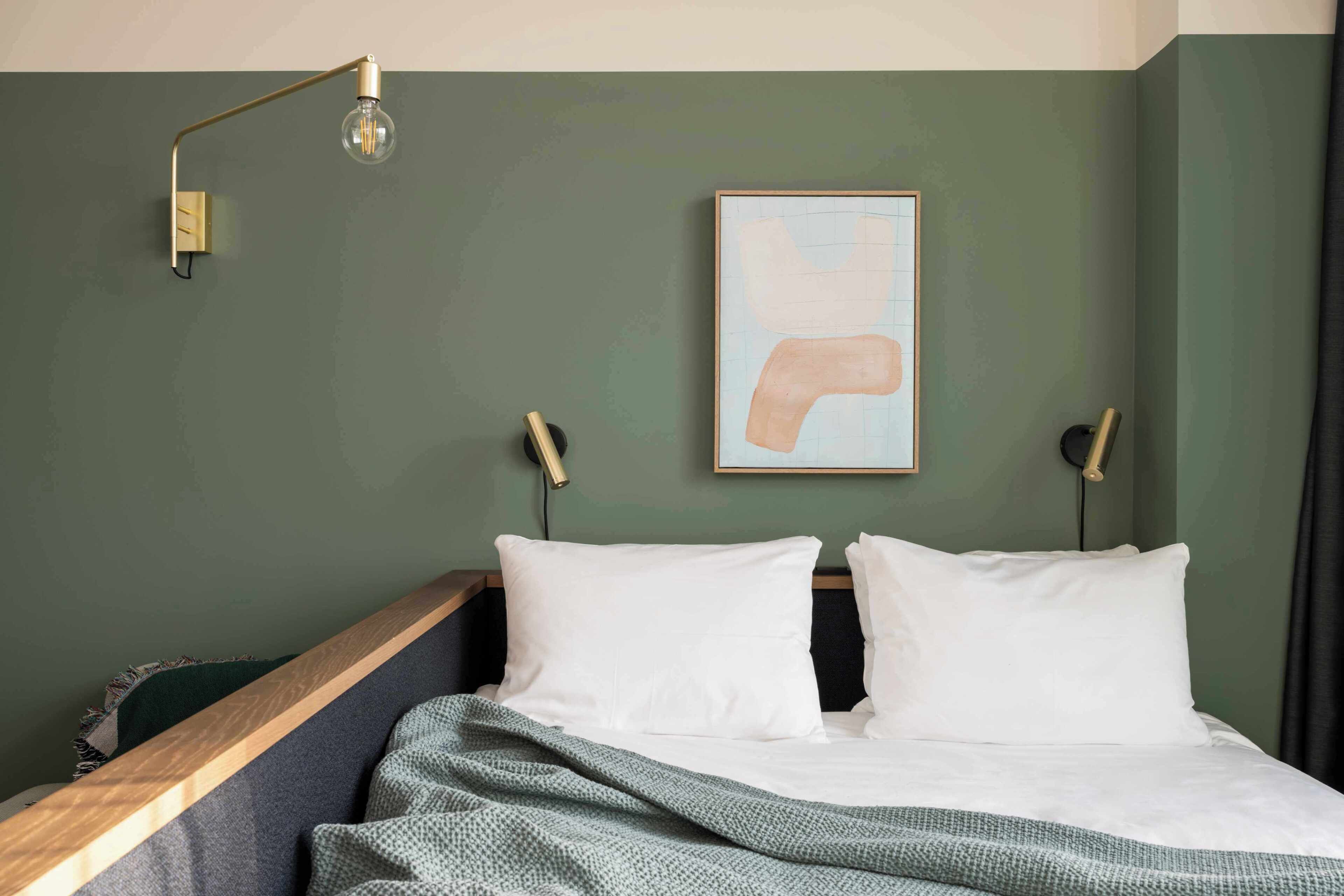 Een bed met witte kussens, een groene deken en een moderne lamp.