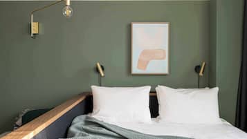 Een bed met witte kussens, een groene deken en een moderne lamp.