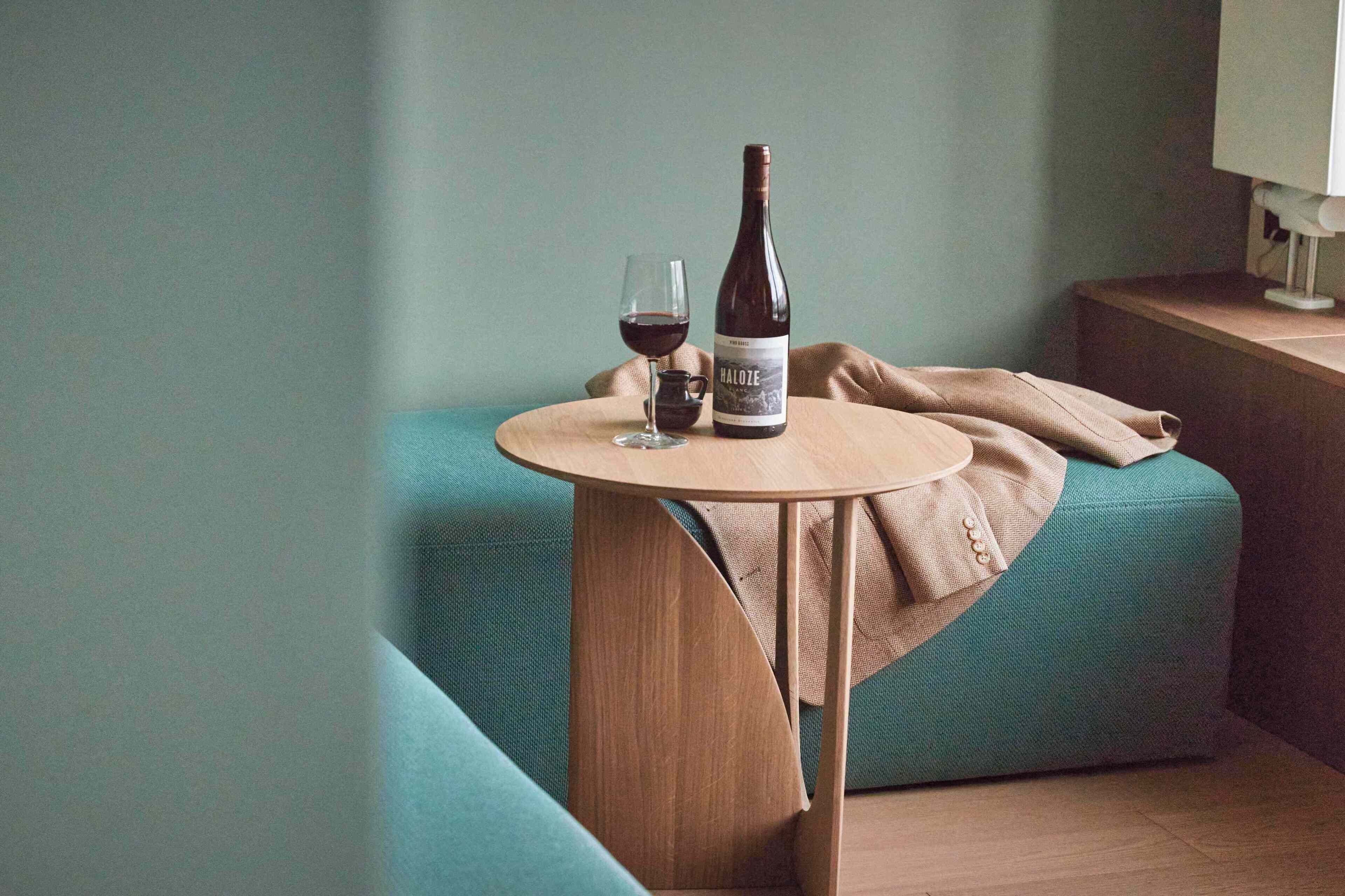 Una habitación con un sofá color turquesa, una mesa de madera con una botella de vino y una copa, y una lámpara en una mesita de noche.