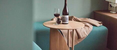 Una habitación con un sofá color turquesa, una mesa de madera con una botella de vino y una copa, y una lámpara en una mesita de noche.