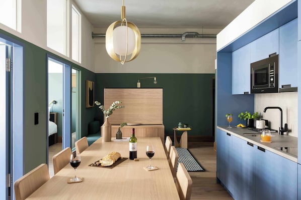 A modern kitchen with a built-in microwave, a dining area with a wooden table and chairs, and a view into the adjacent living space.