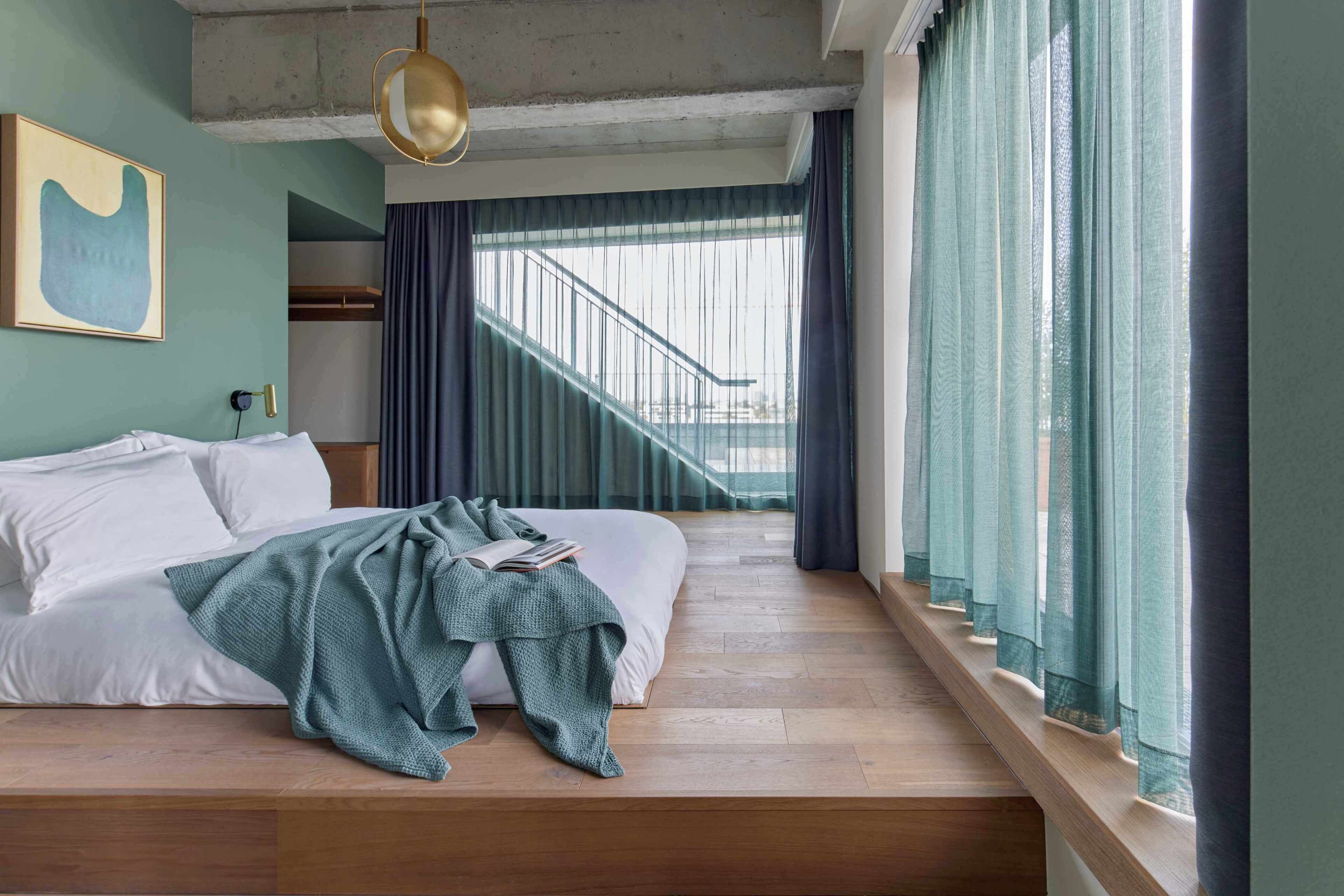 A bedroom with a bed, a window with curtains, a staircase, and a painting on the wall.