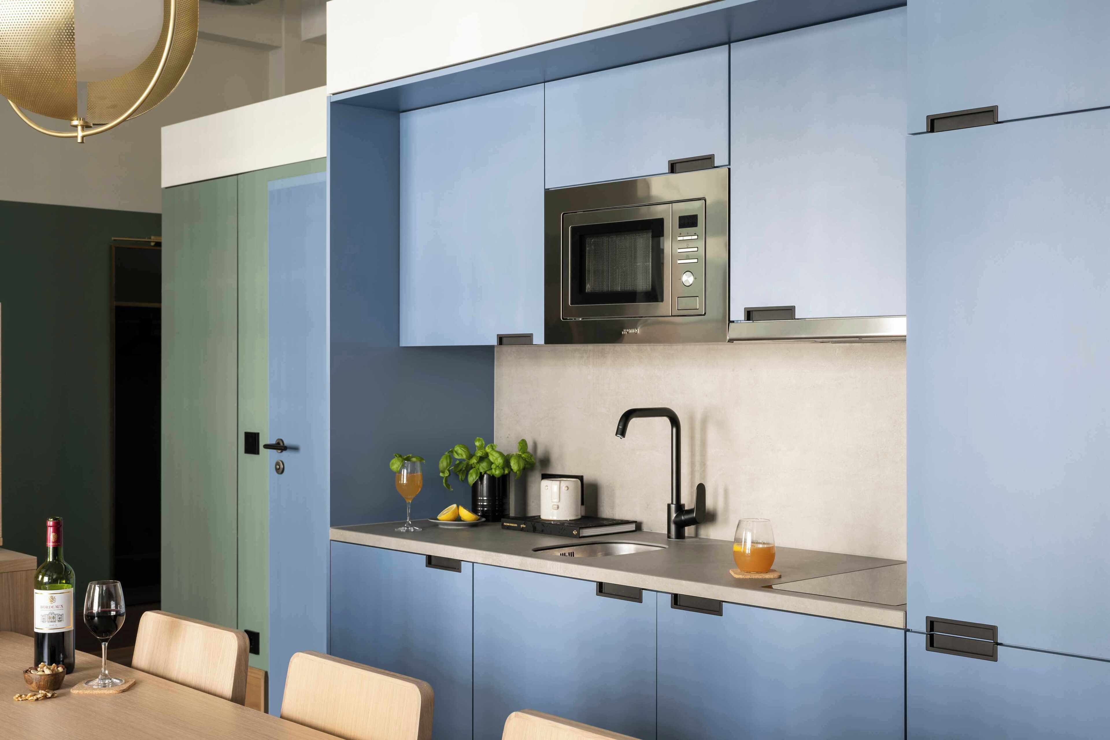 Una cocina moderna con microondas integrado, un lavamanos y una encimera con una botella de vino, una copa y una frutera.
