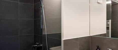 Un baño moderno con ducha envuelta en vidrio, un lavabo blanco y un espejo.