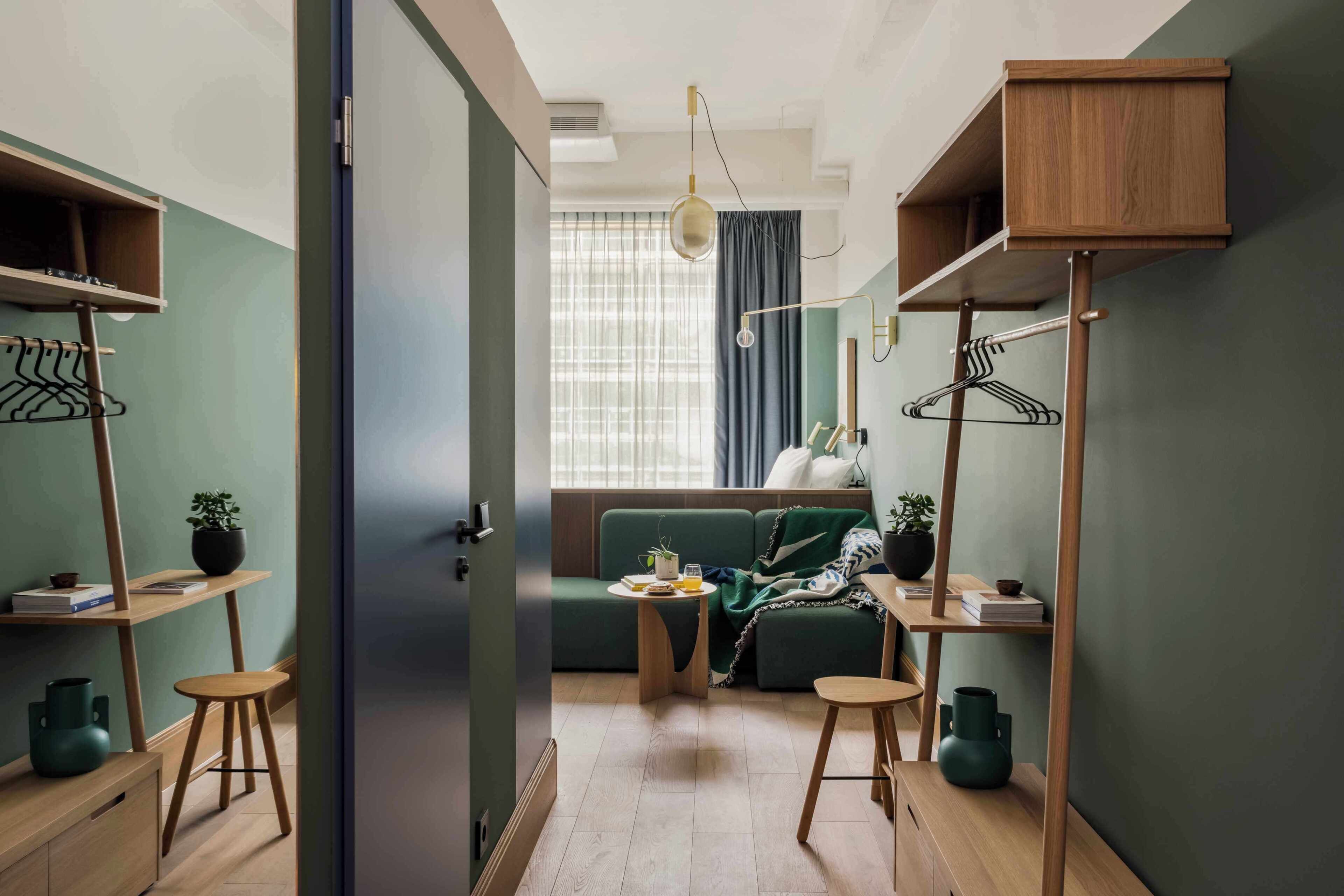 A compact living space with a sofa, a small table, a hanging light fixture, and a coat rack.