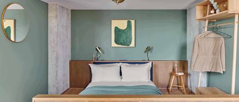 A bedroom with a wooden bed, a bedside table, a hanging light fixture, a mirror, and a wall-mounted shelf.