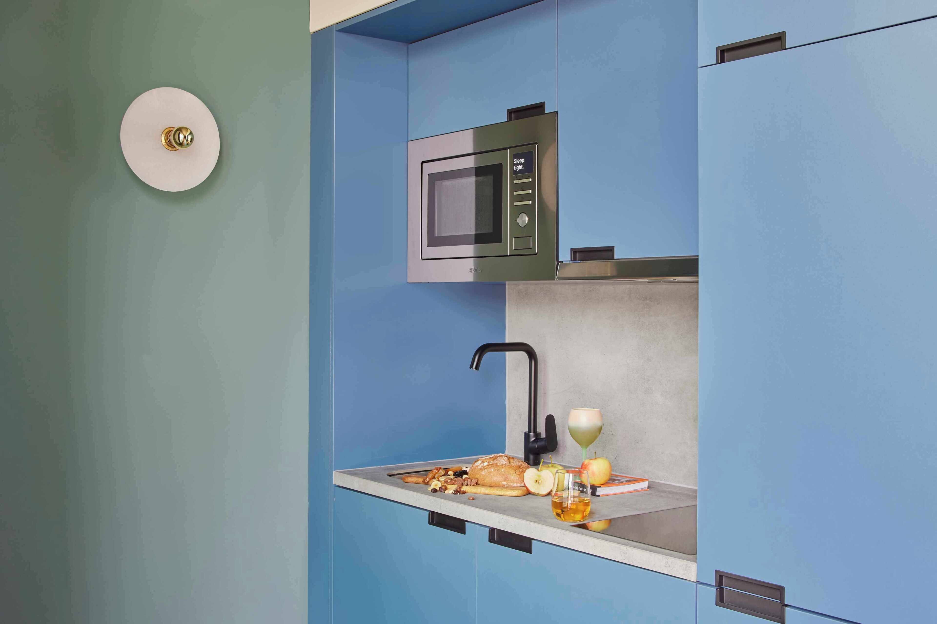 Una cocina con microondas integrado, un fregadero y una pequeña encimera con alimentos y bebidas.