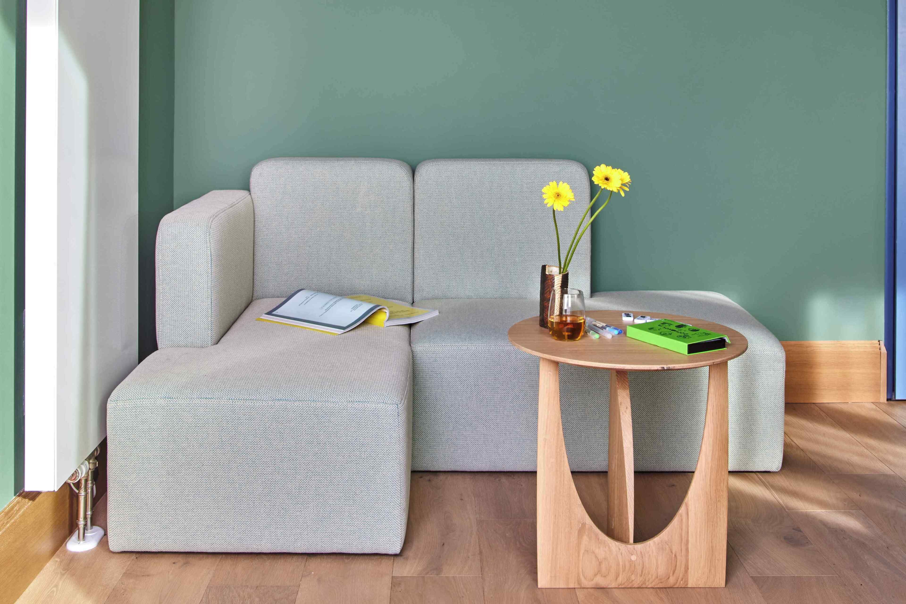 Ein modernes Wohnzimmer mit einem grauen Sofa, einem kleinen Holztisch und einer Vase mit gelben Blumen.