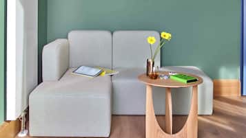 Ein modernes Wohnzimmer mit einem grauen Sofa, einem kleinen Holztisch und einer Vase mit gelben Blumen.