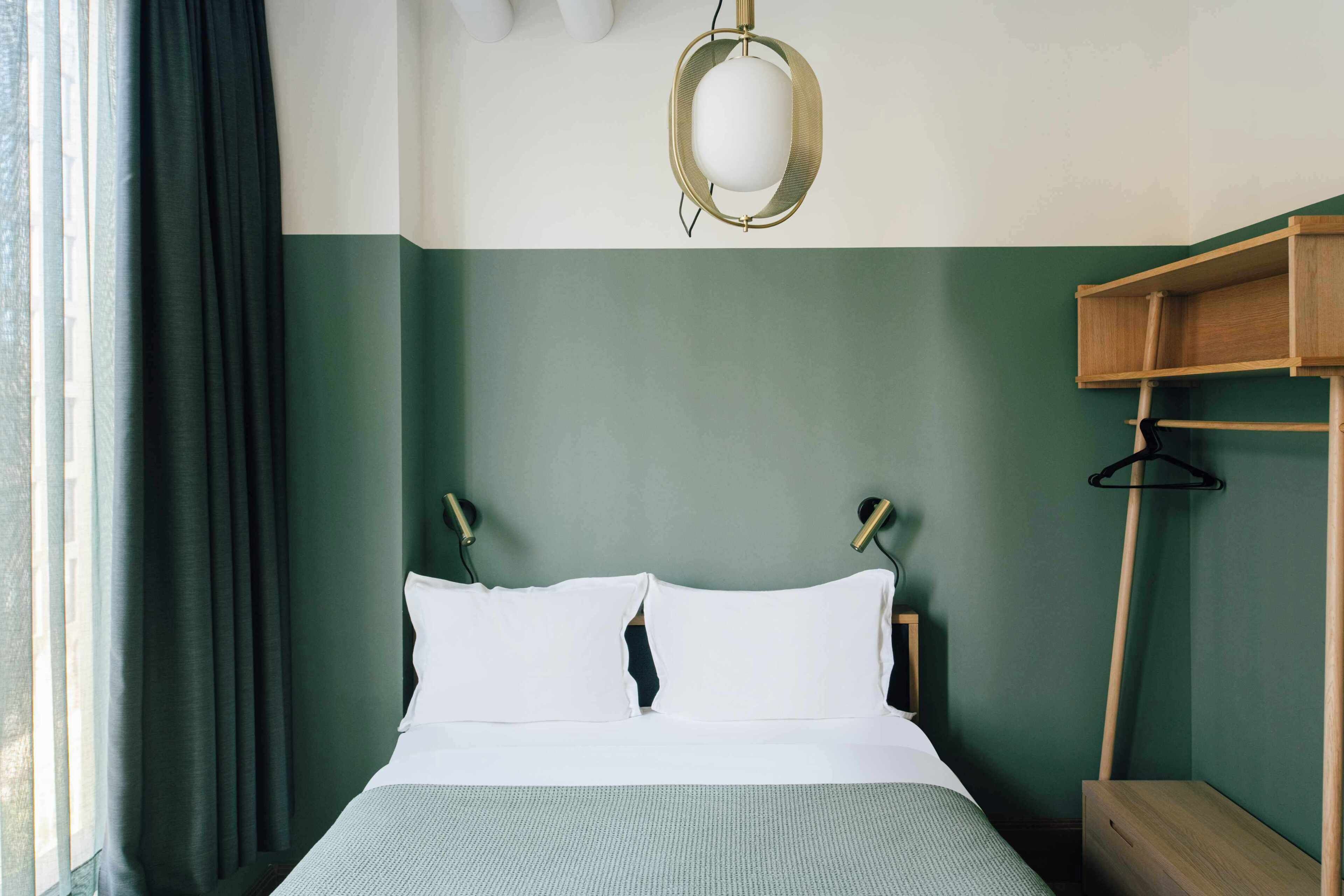 Una cama con ropa de cama blanca, una lámpara colgante y una mesita de noche de madera.
