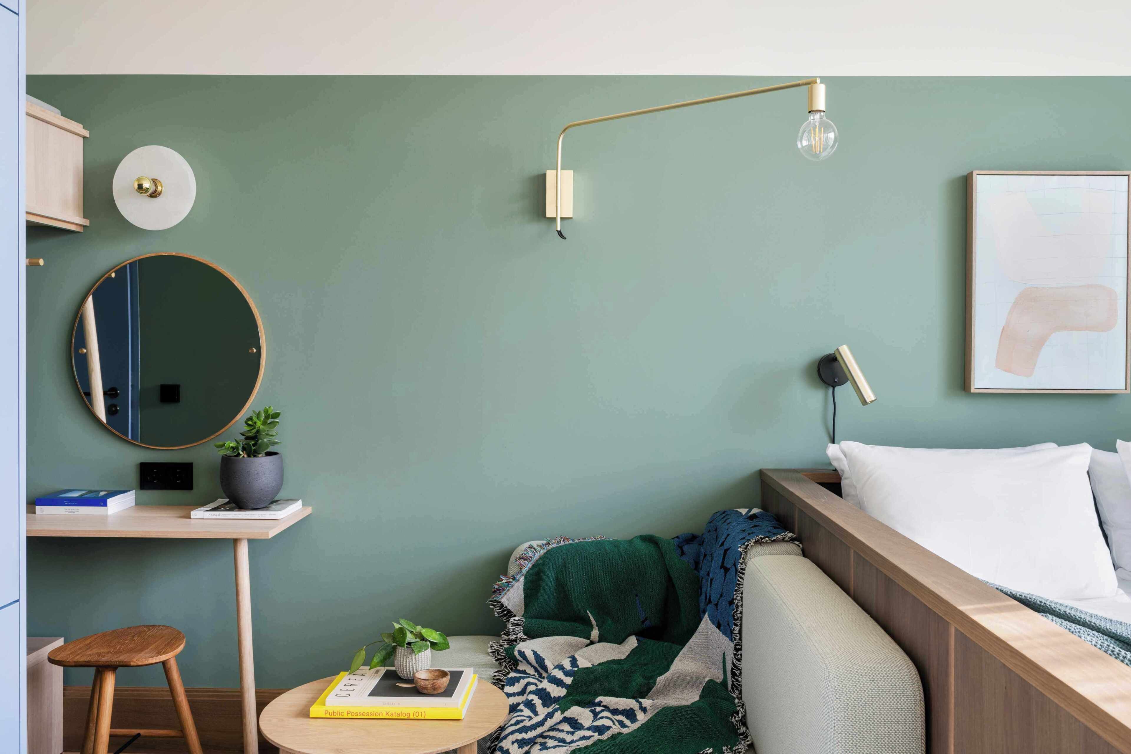 A bedroom with a bed, bedside table, lamp, and a wall-mounted mirror.