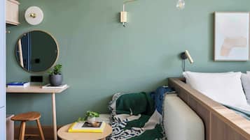 Un dormitorio con cama, mesita de noche, lámpara y un espejo fijado a la pared.