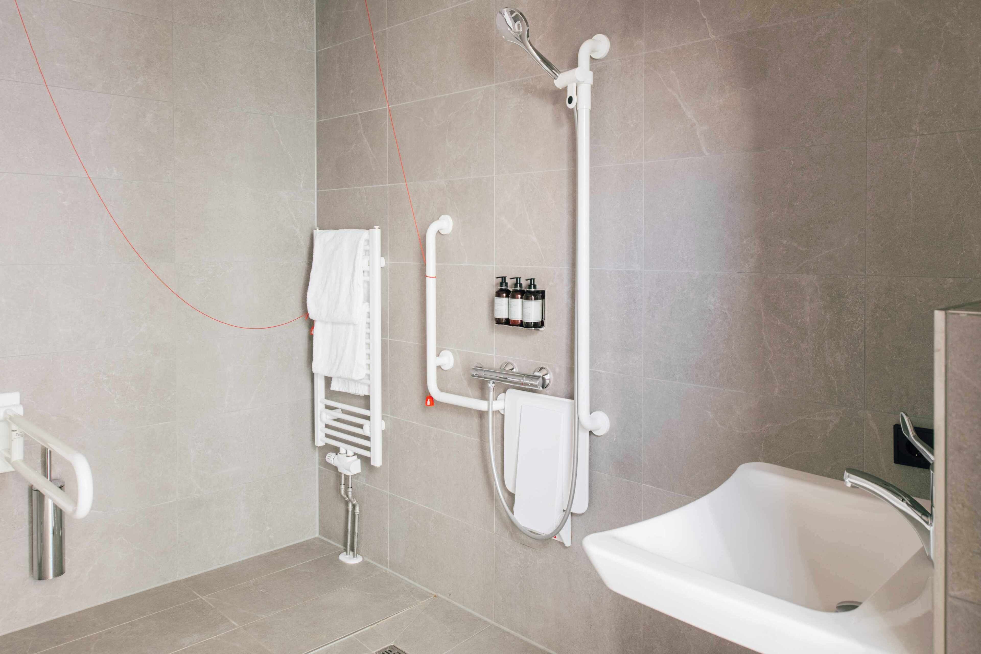 A modern bathroom with a bathtub, a shower with a handheld showerhead, a towel rack, and a hand dryer.