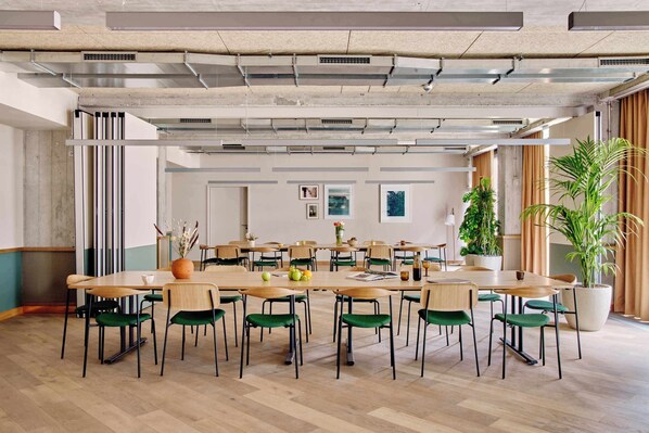 A spacious meeting room with long tables, green chairs, and potted plants.