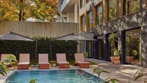 A pool area with lounge chairs and umbrellas, surrounded by a wooden fence and potted plants. - WunderLocke Munich (Munich)